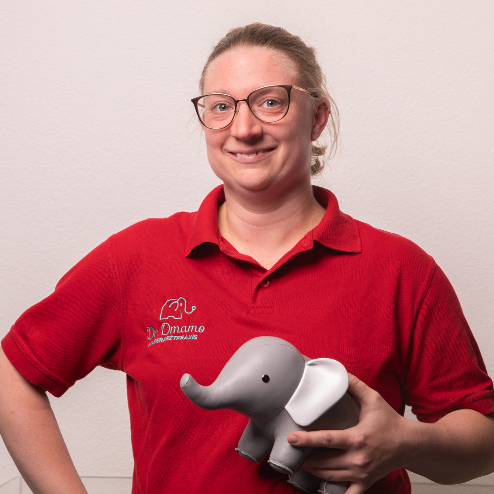 Personalbild der Mitarbeiterin Lisa Krieger, die das Praxismaskottchen, einen kleinen Spielzeugelefanten, hochhält.